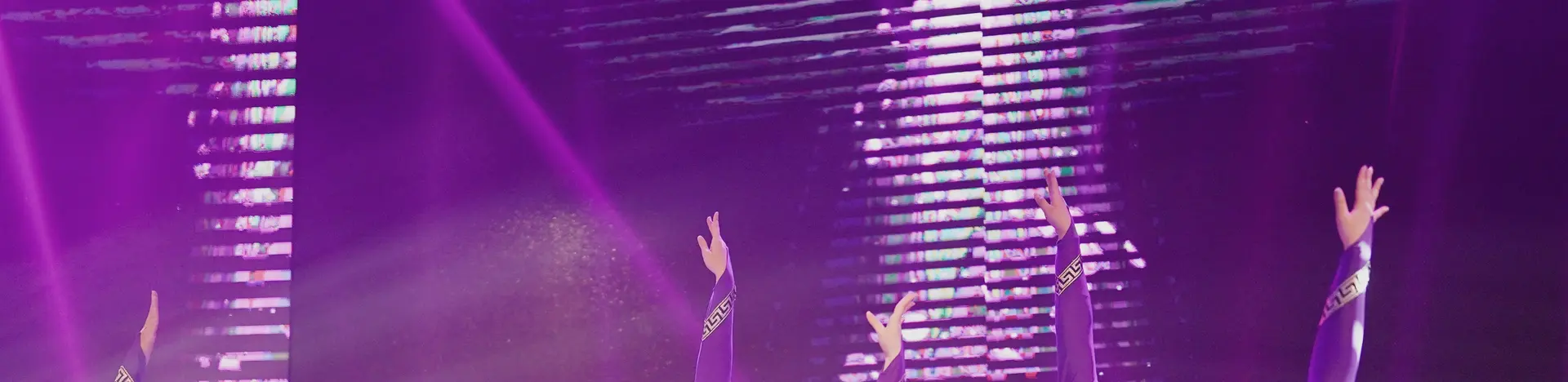 Raised arms on stage in purple light, an LED screen behind