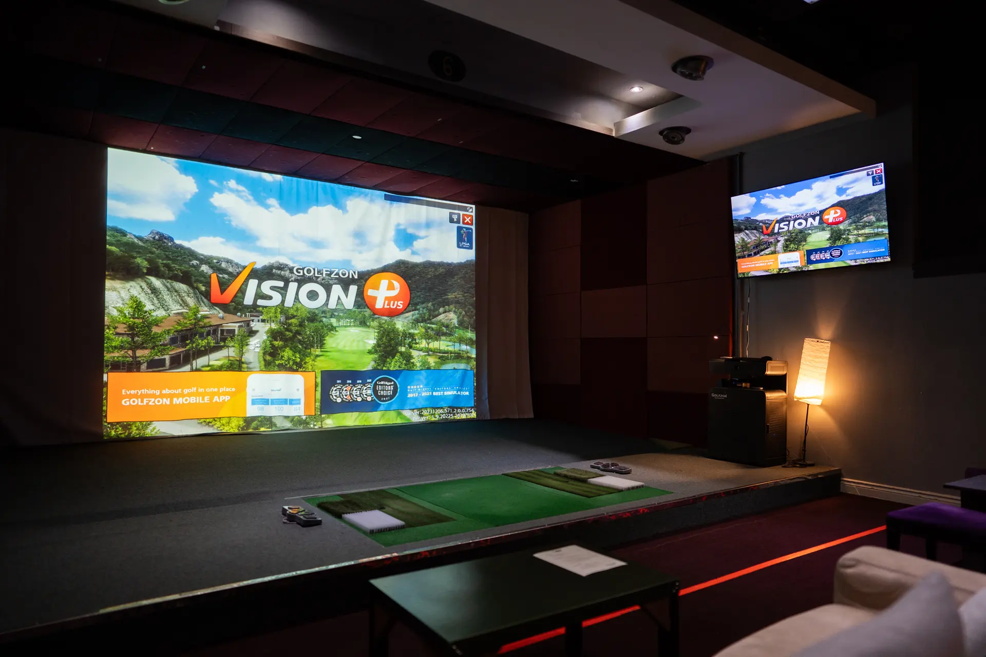 A GolfWing simulator bay: the projection screen, the hitting mat, a wall screen and one floor lamp