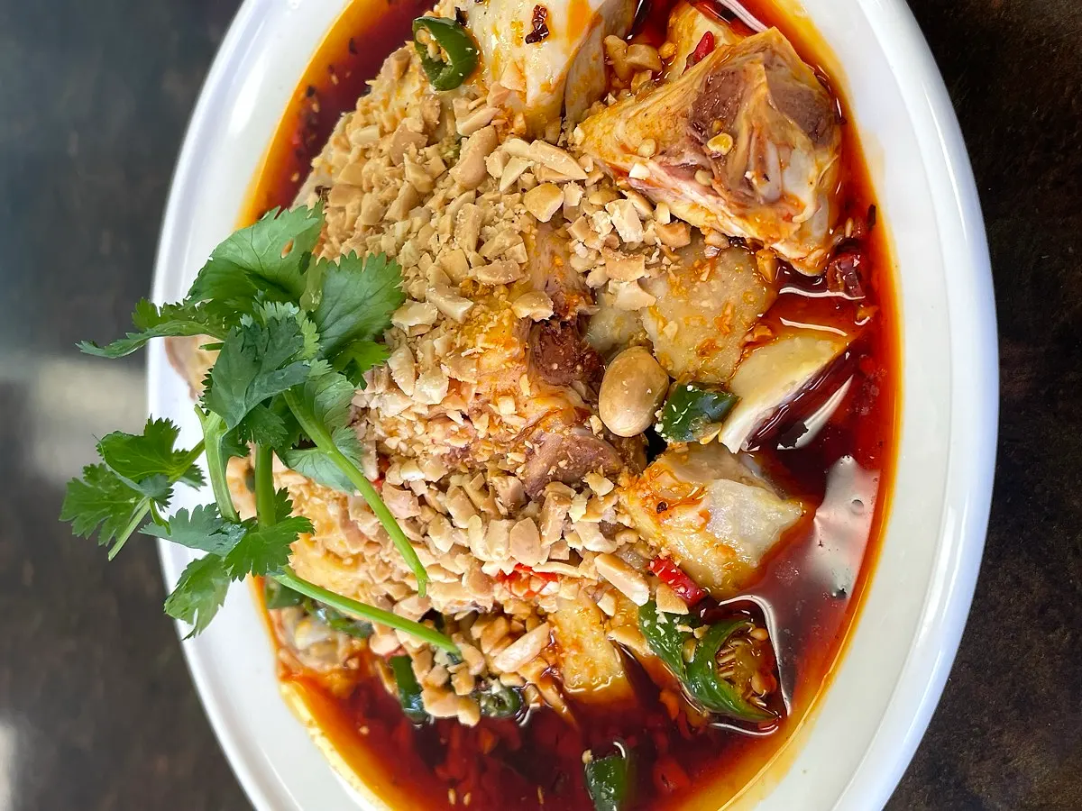 A dish in red chilli oil, topped with crushed peanuts and coriander