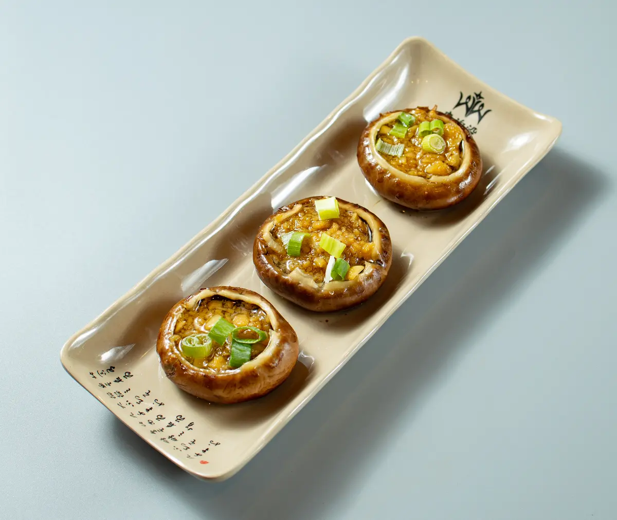 Studio shot: three garlic mushrooms on the restaurant’s long plate, against pale blue