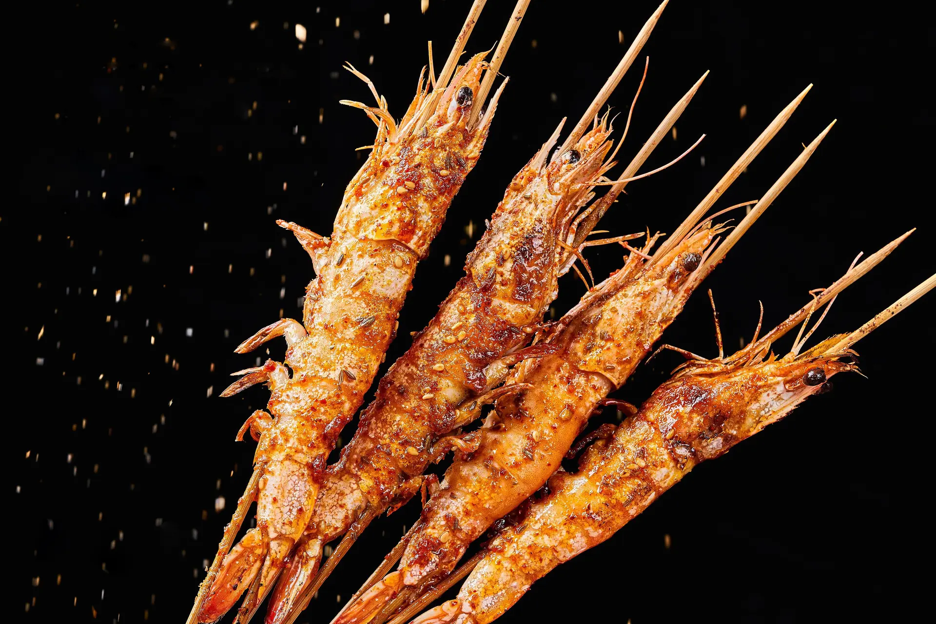 Four grilled prawn skewers on black, dusted with chilli