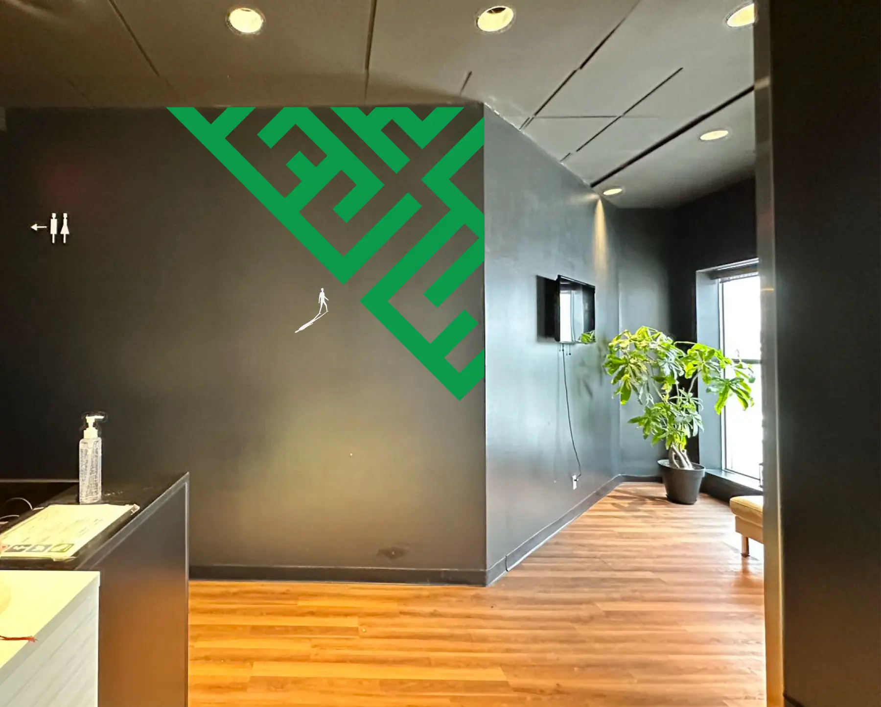 The lobby: a green maze runs down from the corner of the charcoal wall, a small white figure walking out of it (preview composited on a photo of the lobby)