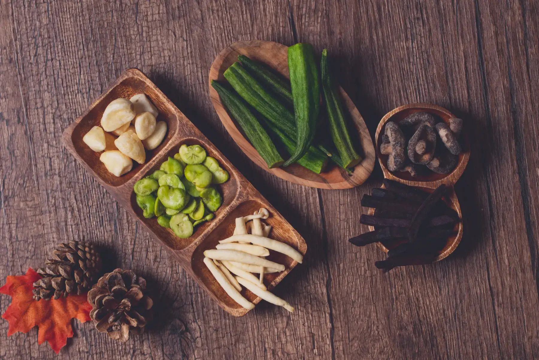 Wooden bowls of garlic, broad-bean, okra, shiitake and purple sweet potato crisps on a wooden table